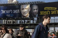 ADDS TRANSLATION OF BILLBOARD - People walk under an election campaign billboard for the Blue and White party, the opposition party led by Benny Gantz, in Ramat Gan, Israel, Tuesday, Feb. 18, 2020. The message next to Gantz, left, says "Looks after Israel." The message next to Prime Minister Benjamin Netanyahu of the Likud party, right, says "Looks after himself." (AP Photo/Oded Balilty)