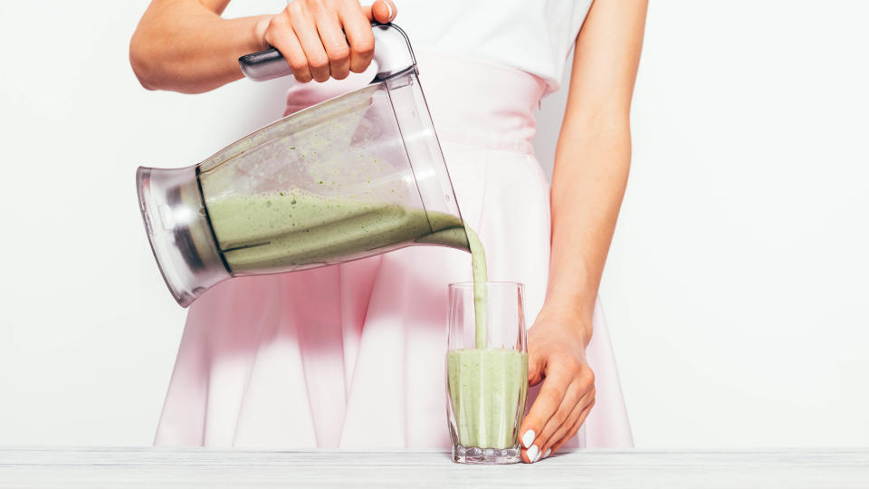 A woman tipping a green smoothie from a blender pitcher into a glass