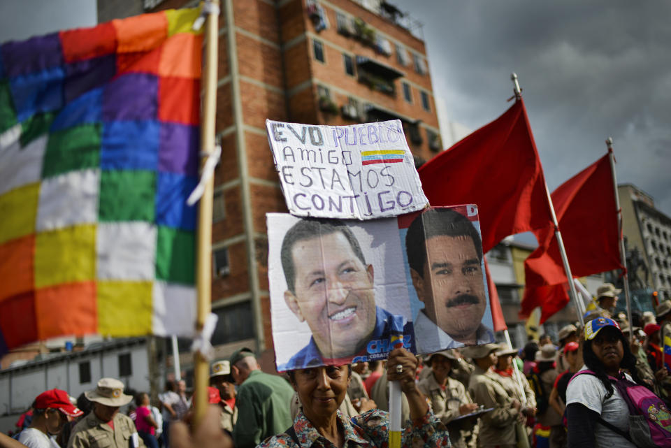 A supporter of Venezuelan President Nicolas Maduro, whose image is held up at right, and late President Hugo Chavez, left, carries the Spanish message: "Evo. People. Friend. We are with you" during a rally in support of former Bolivian President Evo Morales in Caracas, Venezuela, Monday, Nov. 11, 2019. Morales stepped down following weeks of massive protests. (AP Photo/Matias Delacroix)