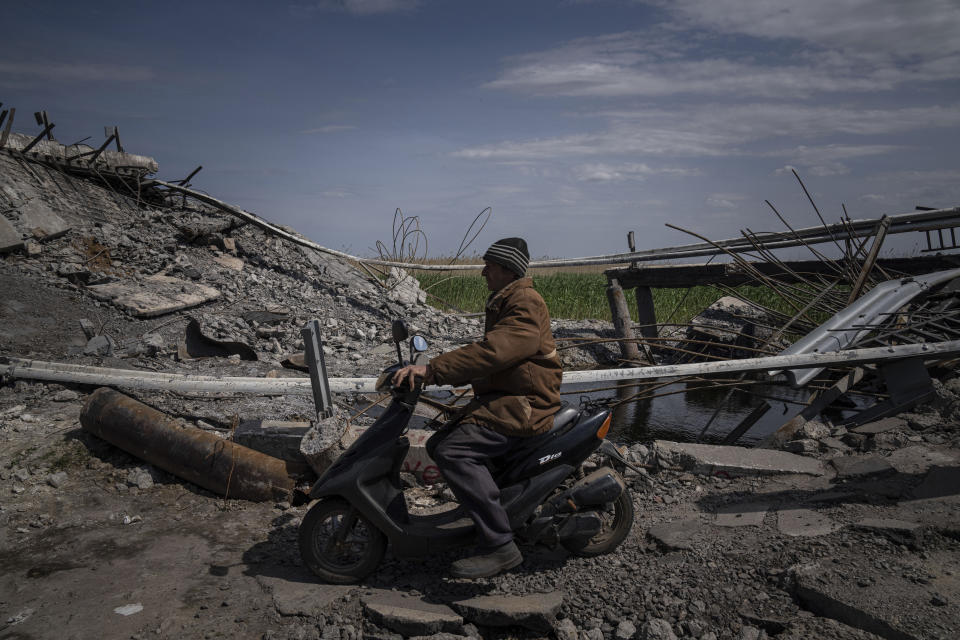 A man drives a scooter next to a bridge destroyed by shelling near Orihiv, Ukraine, Thursday, May 5, 2022. (AP Photo/Evgeniy Maloletka)