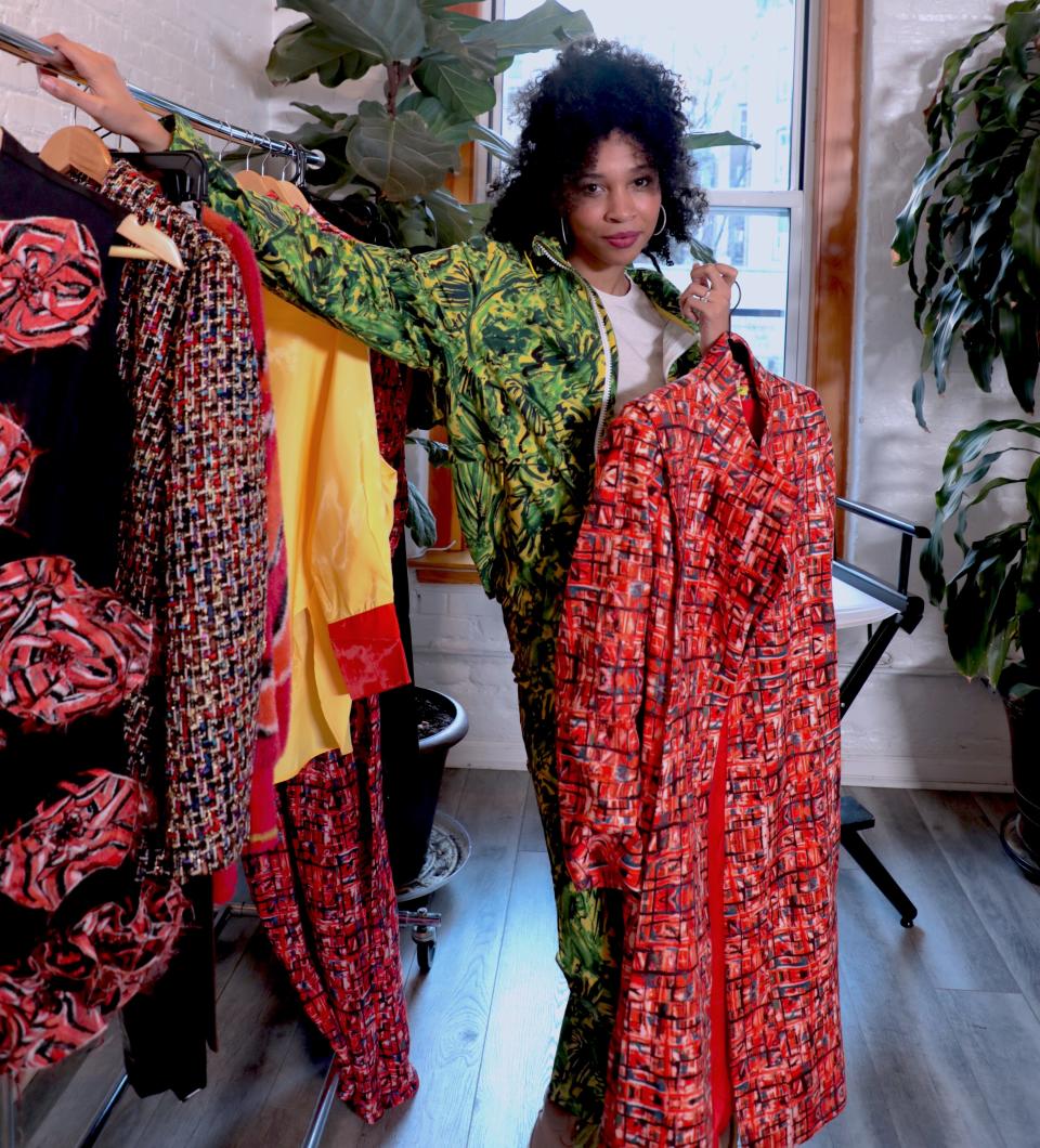 Marrisa Wilson holds a red printed longline jacket while leaning against a rack of clothing.