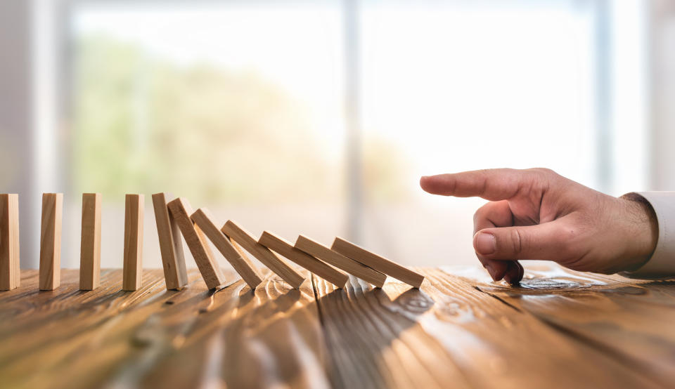 A finger pushes over a line of dominoes.