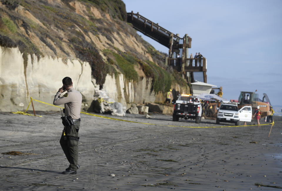 A San Diego County Sheriff's deputy looks on as search and rescue personnel work at the site of a cliff collapse at a popular beach Friday, Aug. 2, 2019, in Encinitas, Calif. At least one person was reportedly killed, and multiple people were injured, when an oceanfront bluff collapsed Friday at Grandview Beach in the Leucadia area of Encinitas, authorities said. (AP Photo/Denis Poroy)