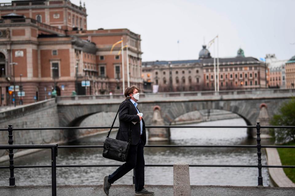 A man wearing a protective mask walks in the rain past the Royal Swedish Opera (at left) in Stockholm, Sweden, on April 27, 2020.