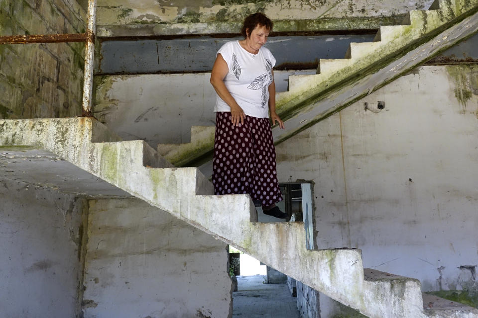 Devla Ajsic walks through the ruins of a former battery factory in Potocari near Srebrenica, Bosnia, Wednesday, July 7, 2021. Ajsic, who fled Srebrenica after being sexually abused in July 1995, has returned to live there, but says she is still afraid to walk through the town because she never knows if the people she encounters in the streets are deniers of the genocide that took place there or even took part in it. (AP Photo/Eldar Emric)