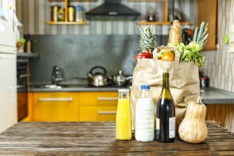 Paper bag with various food is on the table in the kitchen.