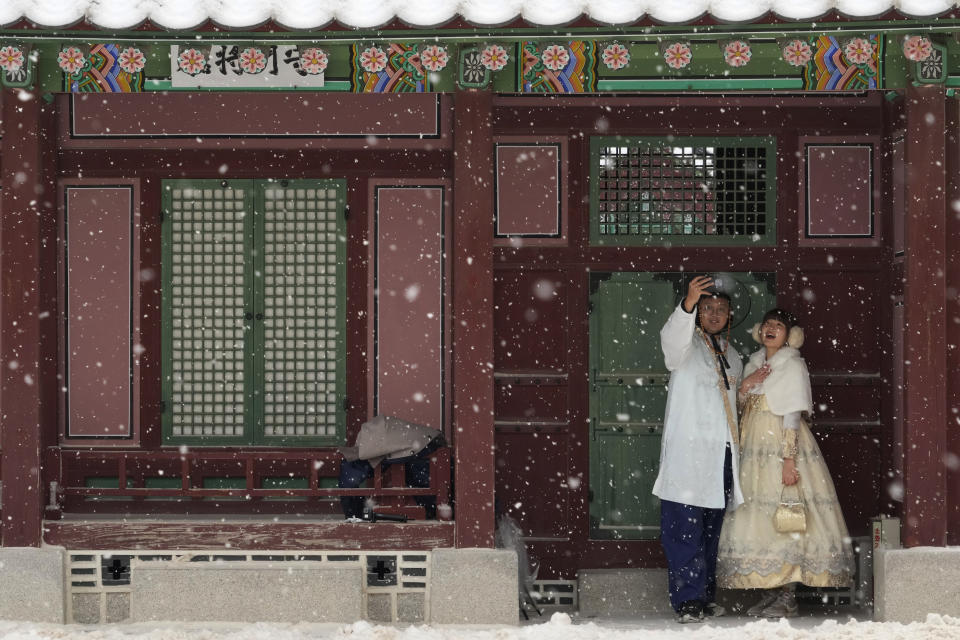 A couple wearing traditional "Hanbok" outfits takes a selfie in the snow at the Gyeongbok Palace, the main royal palace during the Joseon Dynasty and one of South Korea's well known landmarks, in Seoul, South Korea, Thursday, Jan. 26, 2023. (AP Photo/Ahn Young-joon)
