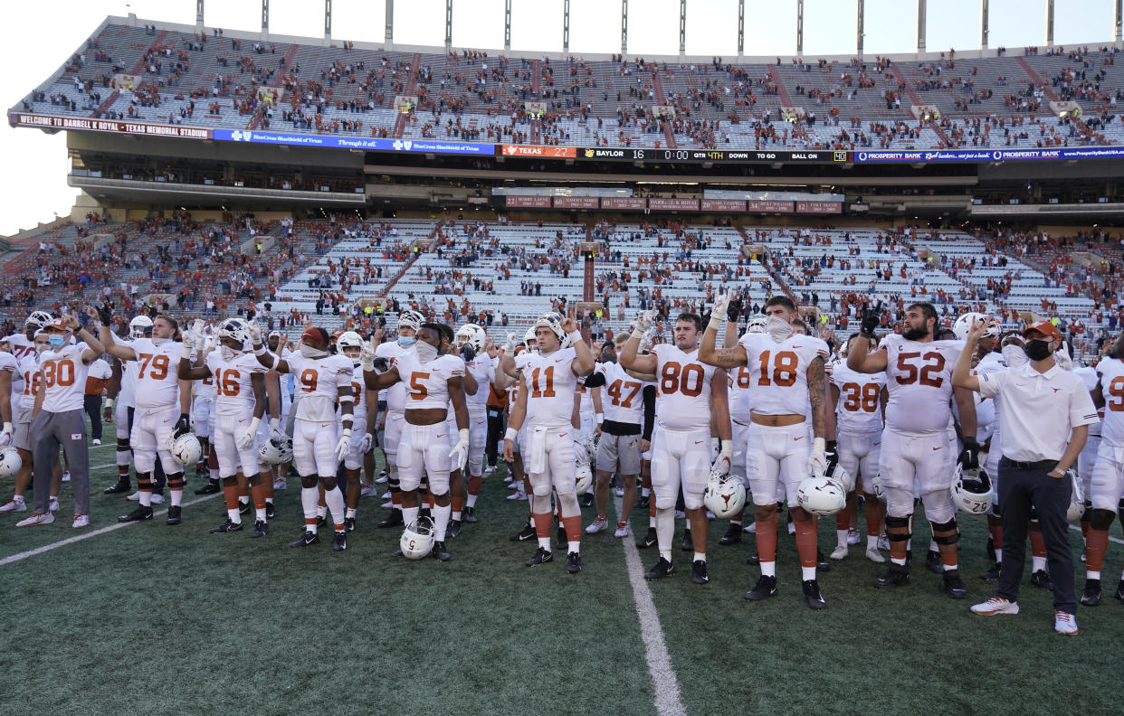 Texas players stand on the football field in front of socially distanced fans in stands. 