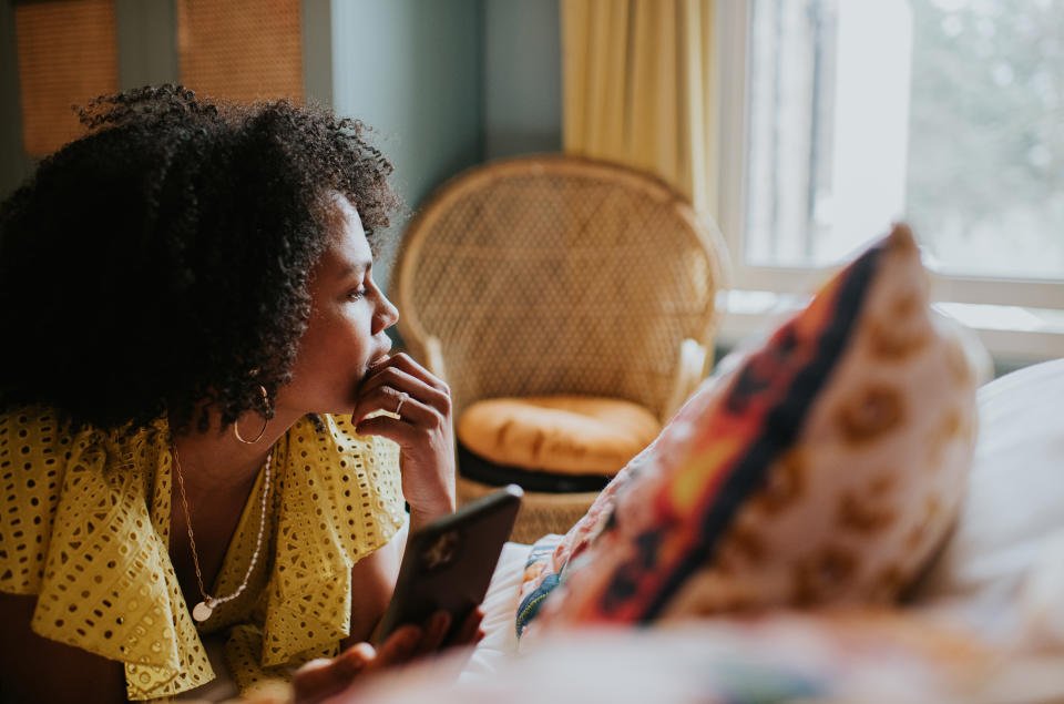 Though love addiction is more common in men, women can also suffer from the condition. (Getty) A woman looks as though she is reflecting on life as she gazes out of a bedroom window. She lies on her stomach on a bed, and touches her chin with her hand. She is holding a smart phone but isn't looking at it.