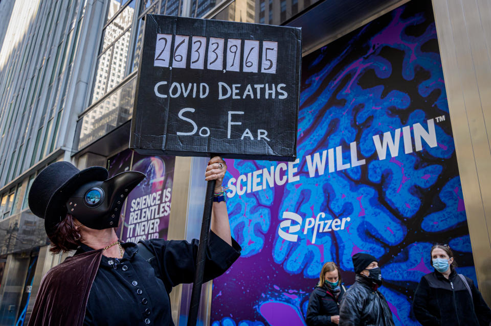 A man wearing a mask and holding a sign is seen protesting for global Covid vaccine distribution. 