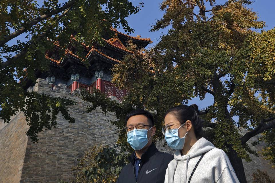 A couple wearing face masks to help curb the spread of the coronavirus walk by the Turret of the Forbidden City in Beijing, Sunday, Oct. 25, 2020. With the outbreak of COVID-19 largely under control within China's borders, the routines of normal daily life have begun to return for its citizens. (AP Photo/Andy Wong)