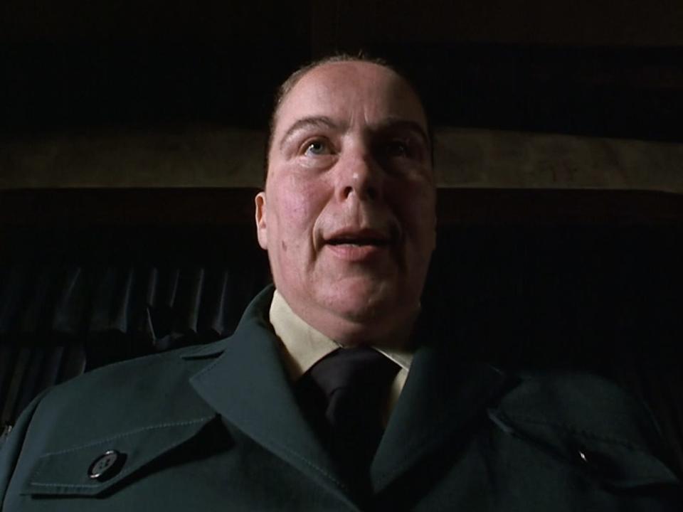 Pam Ferris as Miss Trunchbull wearing a green uniform with a black tie and hair pulled back severely