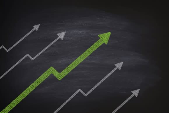 Several arrow charts on a chalkboard indicating gains, with a fatter green arrow in the middle.