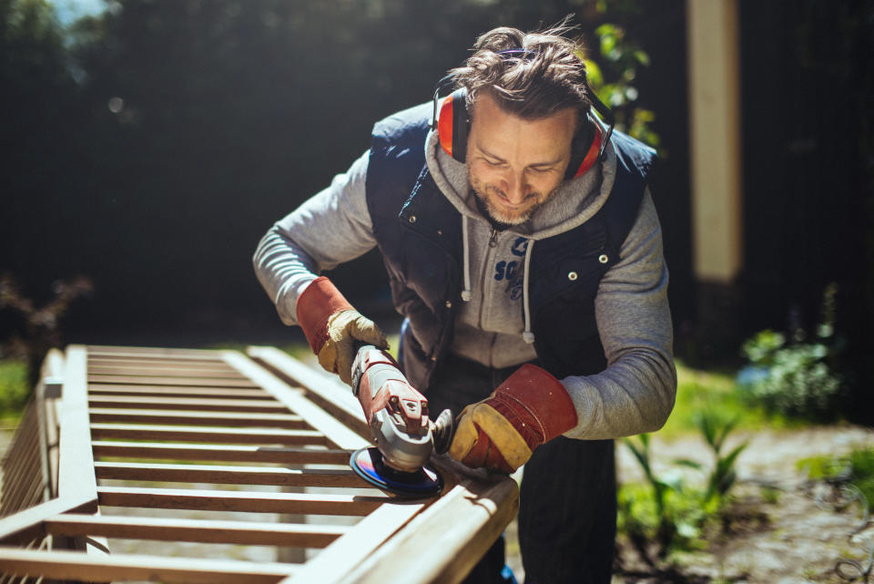 Smiling man grinding an old handrail in the garden.