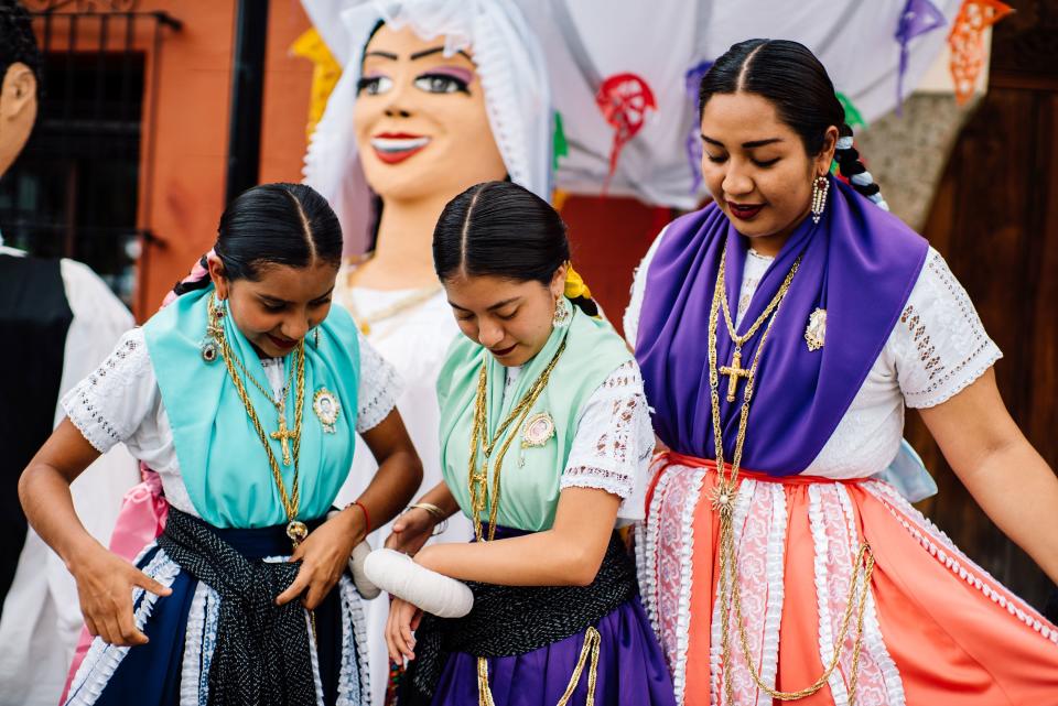 Girls who were part of a wedding party outside the Temple of Santo Domingo in central Oaxaca City, checking on their garments. Behind them is one of the traditional Oaxacan Monos de Calenda, giant papier-mâché puppets representing the bride and groom that dance in procession with the wedding party.