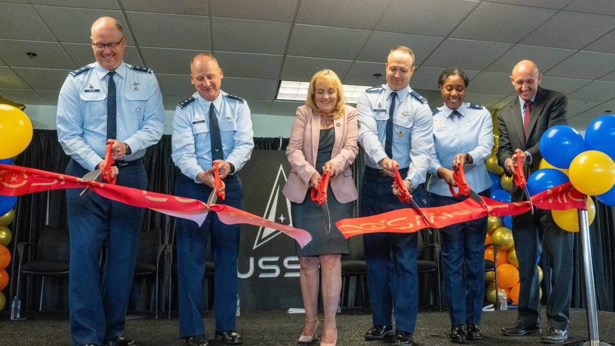  people in blue military uniforms cut a ribbon in an office 