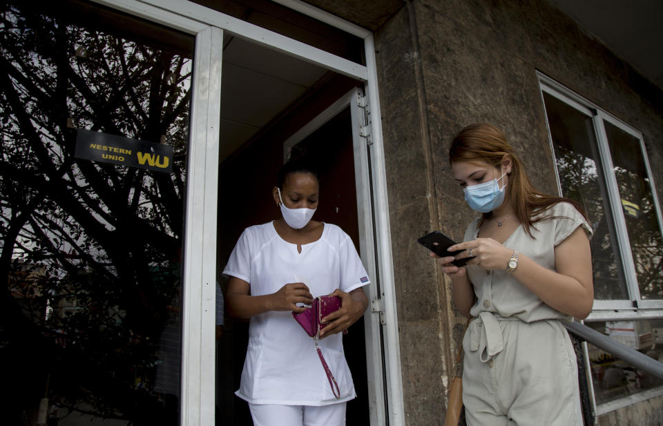 A Cuban health worker leaves a Western Union office after collecting money as another client waits her turn on the office's last day of business in Havana, Cuba, Monday, Nov. 23, 2020. Restrictions from the Trump administration on the military-controlled operator that handles cash deposits will go into effect Monday at 6 p.m. local, keeping Cubans from being able to retrieve money sent from abroad through Western Union – the main source of cash remittances for many families. (AP Photo/Ismael Francisco)