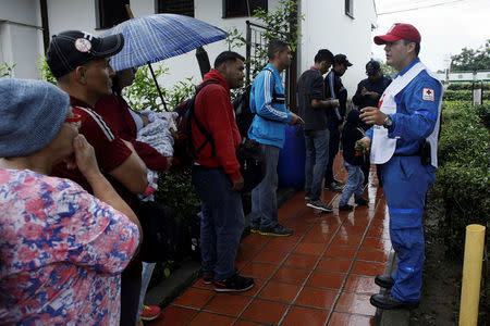 A member of the Colombian Red Cross explains the requirements to be able to attend the Transitory Attention Center to the Migrant, to people queuing to stamp their passports at the migration office in Cucuta, Colombia February 13, 2018. REUTERS/Carlos Eduardo Ramirez