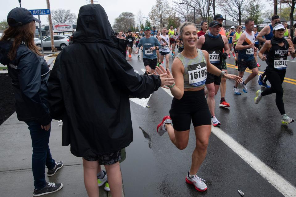 Katie Jones, of South Dakota, gets high-fives as she runs down Waverly Street (Route 135) during the 127th running of the Boston Marathon, April 17, 2023.