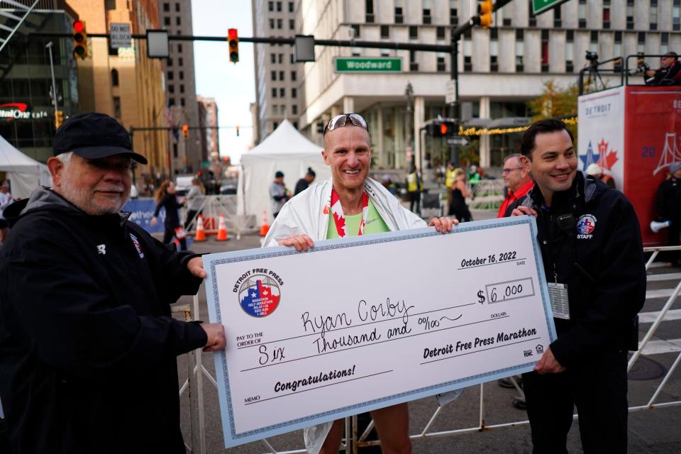 Detroit Free Press Editor and Vice President Peter Bhatia, left, and Detroit Free Press executive race director Aaron Velthoven present the first place check to Ryan Corby of Novi after he crosses the finish line in first place for the men during the full marathon during the 45th Annual Detroit Free Press Marathon in Detroit on Sunday, October 16, 2022.