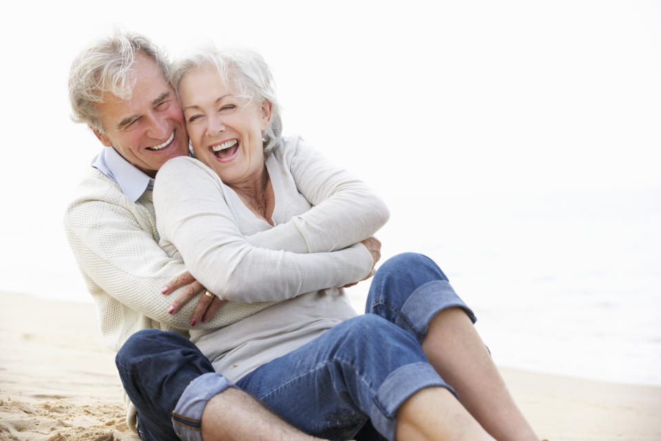 Senior Couple Sitting On Beach Together Laughing