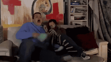 A gif showing a man and woman on the sofa, screaming at a movie and throwing popcorn everywhere