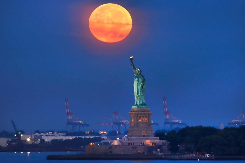 <p>Gary Hershorn/Getty Images</p> The full Harvest Moon sets behind the Statue of Liberty as the sun rises on September 10, 2022, in New York City.