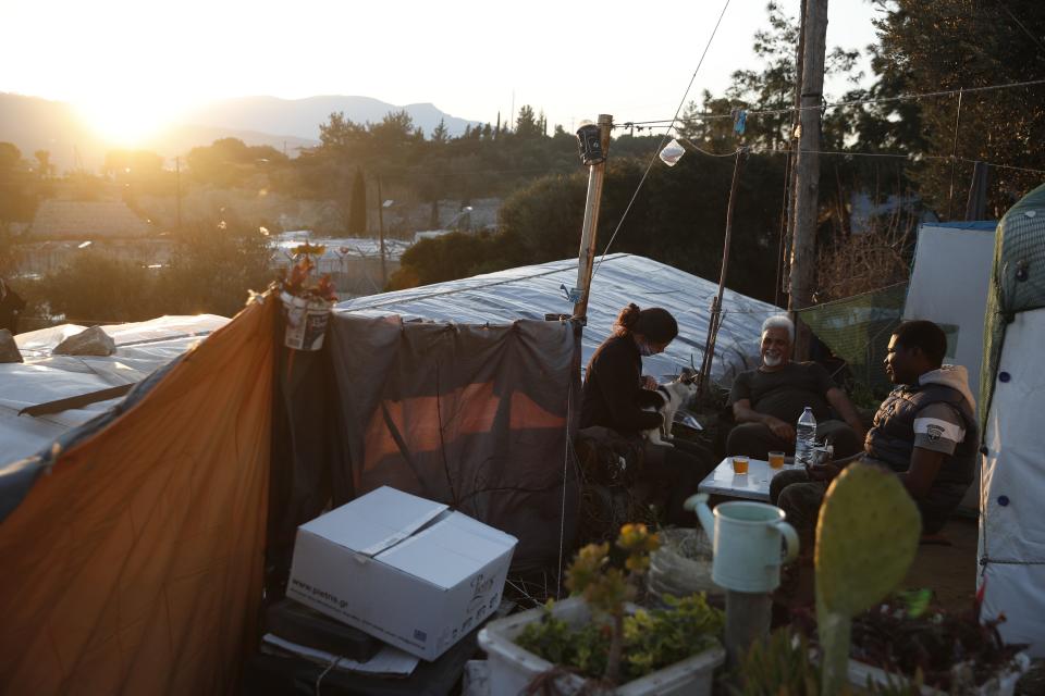 Migrants sit outside of a makeshift tent as the suns sets outside the perimeter of the overcrowded refugee camp at the port of Vathy on the eastern Aegean island of Samos, Greece, Tuesday, Feb. 23, 2021. On a hill above a small island village, the sparkling blue of the Aegean just visible through the pine trees, lies a boy’s grave. His first ever boat ride was to be his last - the sea claimed him before his sixth birthday. His 25-year-old father, like so many before him, had hoped for a better life in Europe, far from the violence of his native Afghanistan. But his dreams were dashed on the rocks of Samos, a picturesque Greek island almost touching the Turkish coast. Still devastated from losing his only child, the father has now found himself charged with a felony count of child endangerment. (AP Photo/Thanassis Stavrakis)