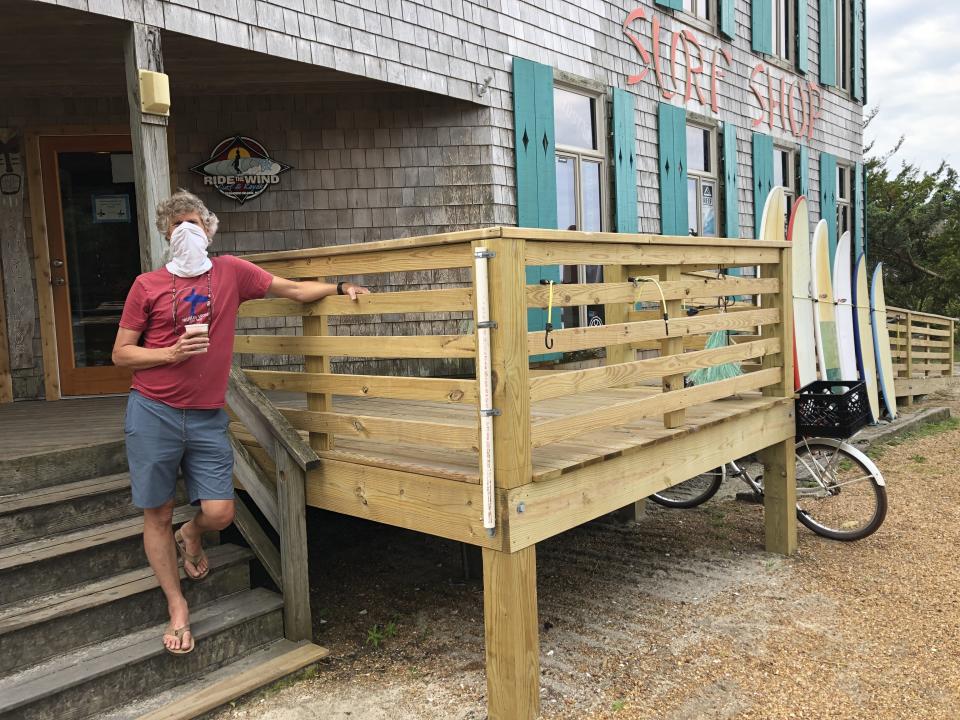 Bob Chestnut stands outside of his Ride the Wind Surf Shop on North Carolina's Ocracoke Island on June 25, 2020. The secluded travel destination was ravaged by Hurricane Dorian in September and then hit with coronavirus-related travel restrictions in the spring. Residents and business owners are hoping to recoup some of their losses as tourists return, albeit in smaller than usual numbers. But they're wary of a possibly busy hurricane season ahead. (AP Photo/Ben Finley)