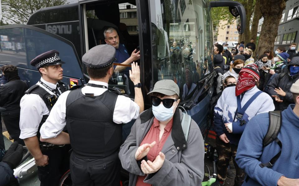 Police officers speak to the bus driver as protesters surround the vehicle