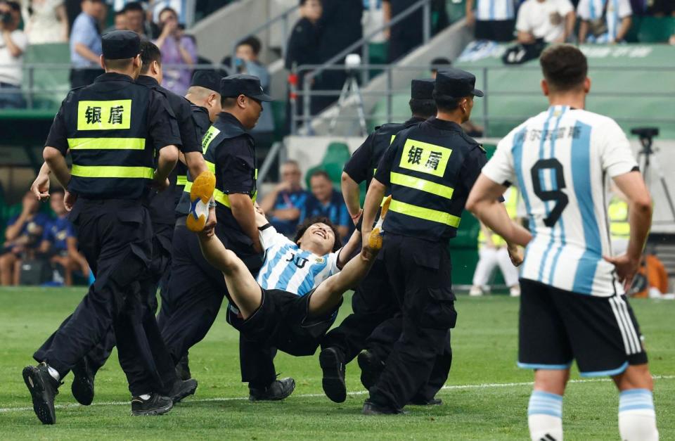 A pitch invader is taken off the pitch by security officials during the match