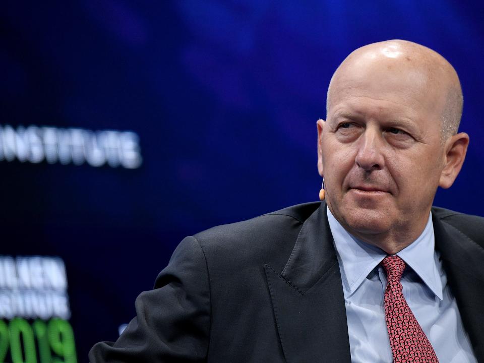 Goldman Sachs CEO David Solomon wears a pale blue shirt and red tie while speaking on stage.