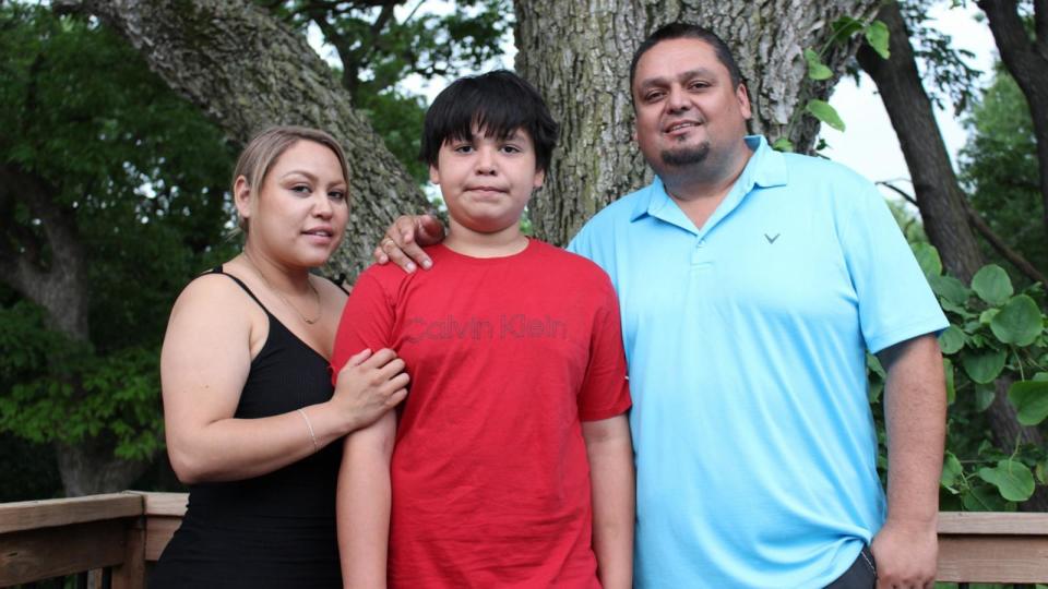 PHOTO: Samuel Arellano stands with his parents, Abigail and Antonio, outside their home in Kansas City, Kansas.  (Bram Sable-Smith/KFF Health News)