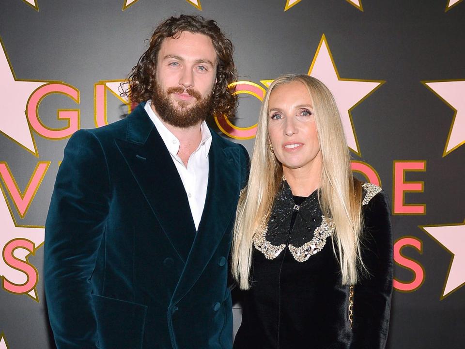 Aaron Taylor-Johnson poses with Sam Taylor-Johnson on a background of pink stars in this photo from November 2021.