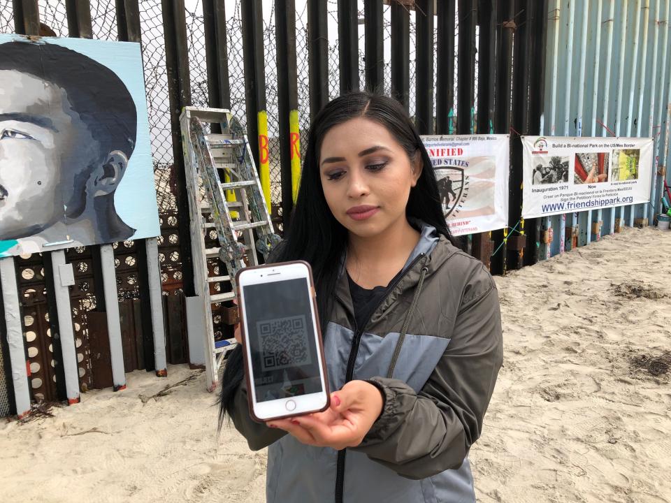 Lizbeth De La Cruz Santana shows a barcode on her mobile phone, part of a new mural on the Mexican side of a border wall in Tijuana, Mexico, Friday, Aug. 9, 2019. De La Cruz Santana conceived the interactive mural in Tijuana as part of doctoral dissertation at the University of California, Davis. The mural shows faces of people deported from the U.S. with barcodes that activate first-person narratives on visitors' phones. (AP Photo/Elliot Spagat)