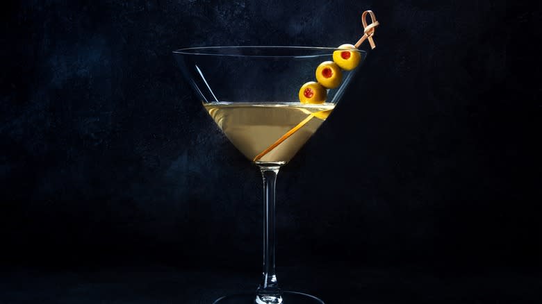 A martini garnished with olives on a black background