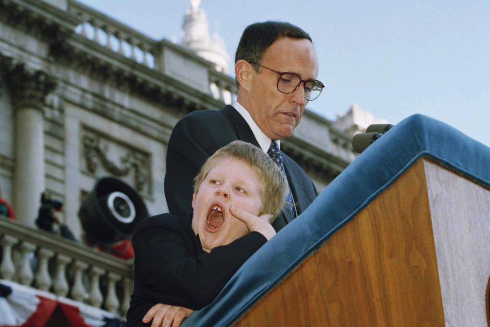 FILE — Andrew Giuliani, left, yawns as his father, New York Mayor Rudolph Giuliani, addresses the crowd after being sworn-in as the 107th Mayor of New York, Jan. 2, 1994. When political kids upstage their parents, it brings a moment of levity to the official workings of government. It’s also a solid case study on the sheer unifying power of humor. (AP Photo/Mike Albans, File)