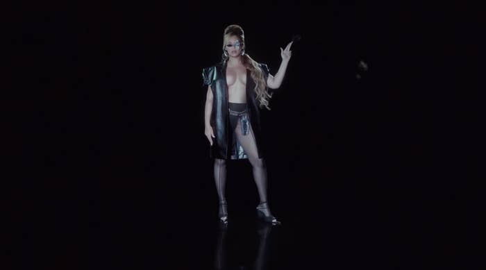 Beyoncé in an edgy open jacket with no shirt underneath and high heels holding  her fingers up as if they are a pistol in a shot from "Texas Hold 'Em"