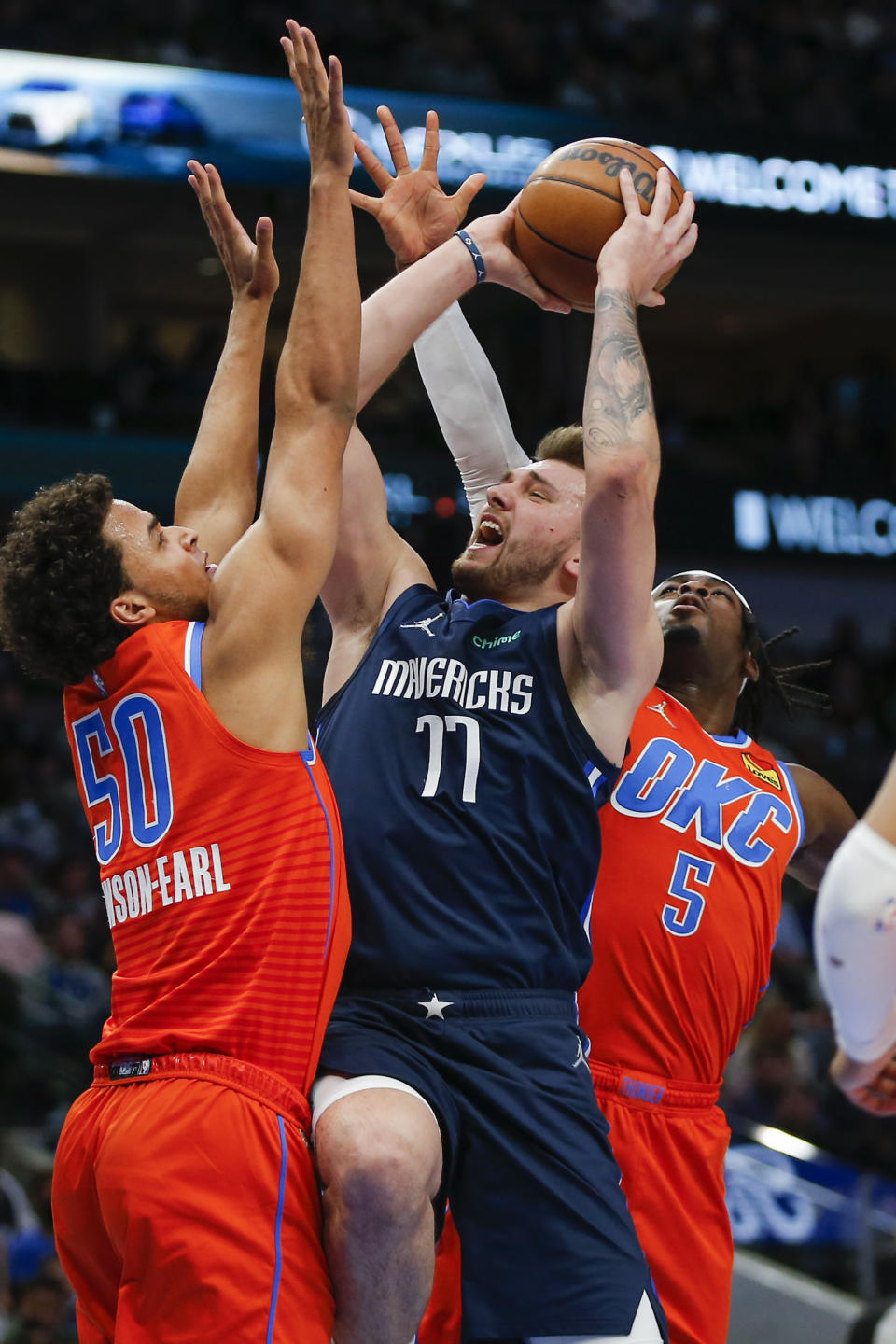 Dallas Mavericks guard Luka Doncic (77) attempts to shoot as Oklahoma City Thunder forwards Jeremiah Robinson-Earl (50) and Luguentz Dort (5) defend during the first half of an NBA basketball game, Monday, Jan. 17, 2022, in Dallas. (AP Photo/Brandon Wade)