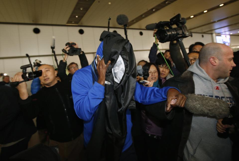 Former NBA basketball player Eric "Sleepy" Floyd covers his face with clothes as journalists chase him upon his arrival from North Korea's Pyongyang, at Beijing Capital International Airport