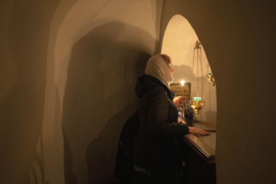 A believer holds a candle as she prays at a sarcophagus with holy relics in the underground labyrinth of the Monastery of the Caves, also known as Kyiv-Pechersk Lavra, one of the holiest sites of Eastern Orthodox Christians, in Kyiv, Ukraine, Friday, March 24, 2023. Tensions are on the rise at a prominent Orthodox monastery in Kyiv where the monks are facing eviction later this month. The Ukrainian government accuses the monks of links to Moscow, even though they claim to have severed ties with the Russian Orthodox Church following Russia's full-scale of invasion of Ukraine. (AP Photo/Efrem Lukatsky)