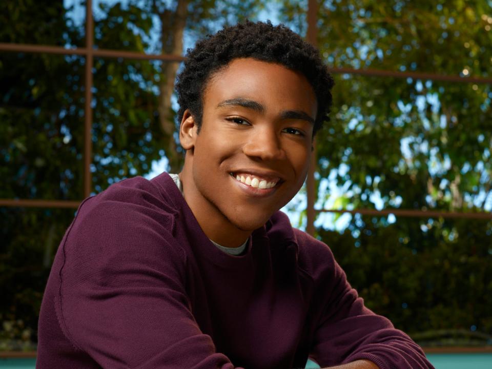 Donald Glover as Troy in season two of "Community." He is smiling with his arms crossed and wears a purple shirt and jeans.