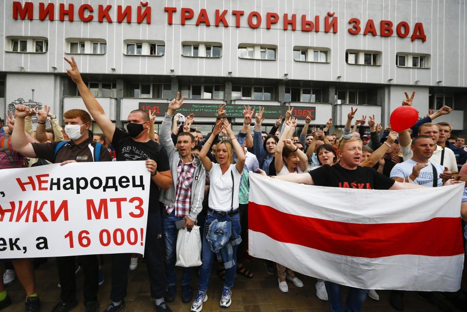 Workers hold an old Belarusian national flag and a banner reading "we are not cattle, we are not sheep, we are workers of MTZ, we are not 20 people, we are 16,000" during a rally in front of the main entrance of the Minsk Tractor Works Plant in Minsk, Belarus, Friday, Aug. 14, 2020. Workers at the plant demanded a new election and called for the release of all those who were detained in a brutal police crackdown on demonstrators challenging the official results of Sunday's presidential vote. (AP Photo/Sergei Grits)