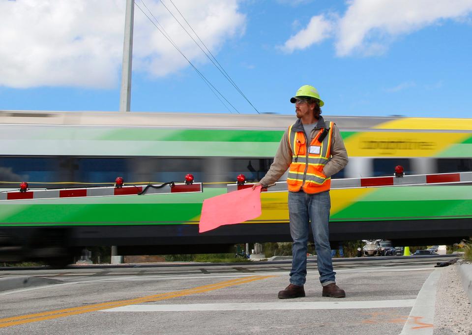 Sean Kearns, of Palm Bay, holds a flag as a Brightline train passes through the intersection of SE Walton Road near Savannas Preserve State Park at 80 mph in Port St. Lucie on Friday, Oct. 21, 2022.