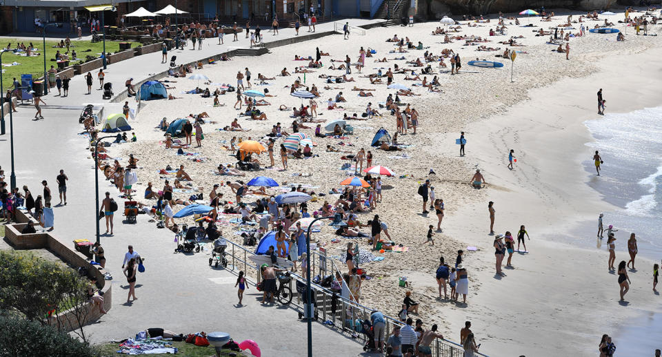 People sitting on the sand and walking at Bronte Beach, NSW on a sunny day.