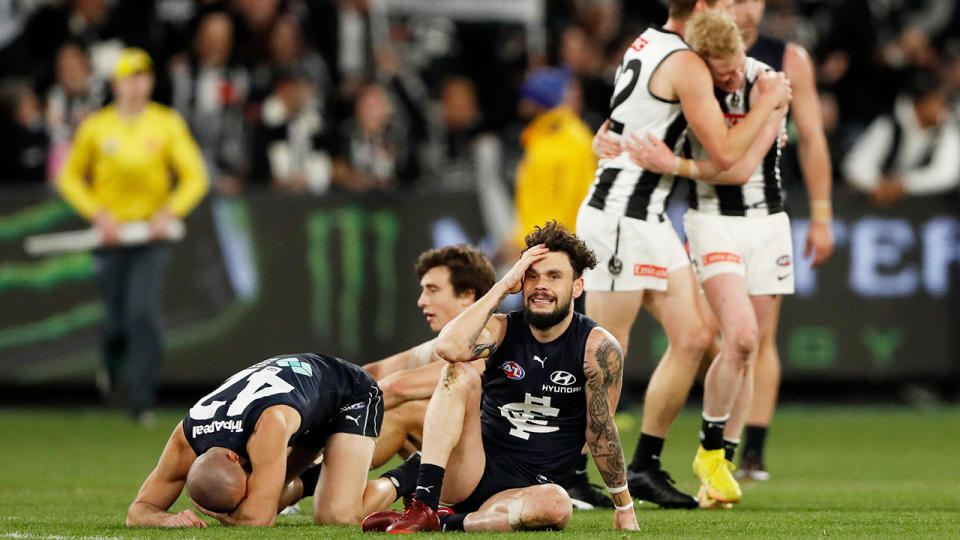 Carlton players react with dismay as Collingwood player celebrate in the background.