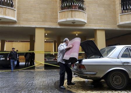 A man puts a carpet on the back of a car near the crime scene where commander Hasan al-Laqqis was killed in the southern Hadath district in Beirut December 4, 2013. REUTERS/Hasan Shaaban