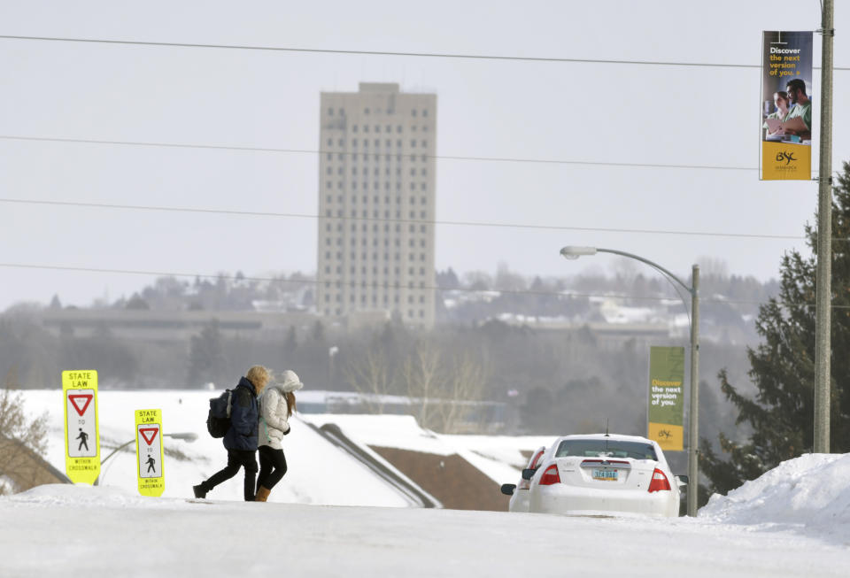 FILE - In this Feb. 7, 2019 file photo, a pair of Bismarck State College students walk across the Bismarck, N.D. campus The state Capitol building is seen in the background. Cities, respectively in North Dakota and Wisconsin, are two of 144 that the federal government is proposing to downgrade from the designation of metropolitan statistical areas, and it could be more than just a matter of semantics. Officials in some of the affected cities worry that raising the bar to 100,000 people could have adverse implications for federal funding and economic development.(Mike McCleary/The Bismarck Tribune via AP, File)