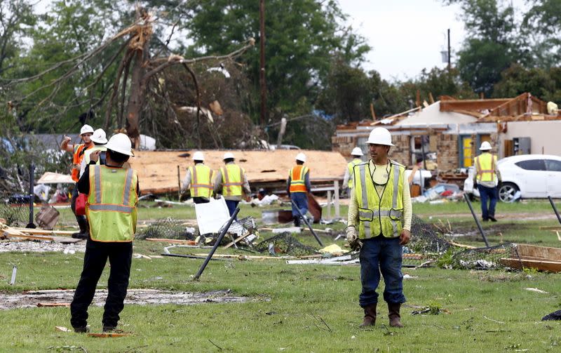A team of workers walk through a neighborhood hit hard by a tornado that swept through the area the previous night in Van, Texas