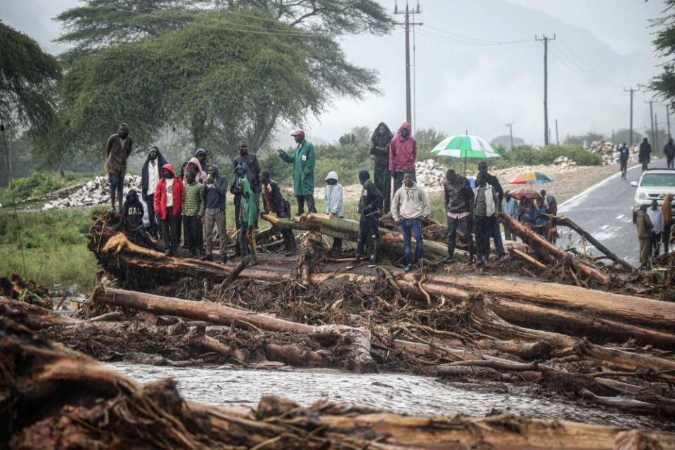 People stand on debris blocking a highway after River Muruny burst its bank following heavy rains in Parua village, in Kenya’s West Pokot county